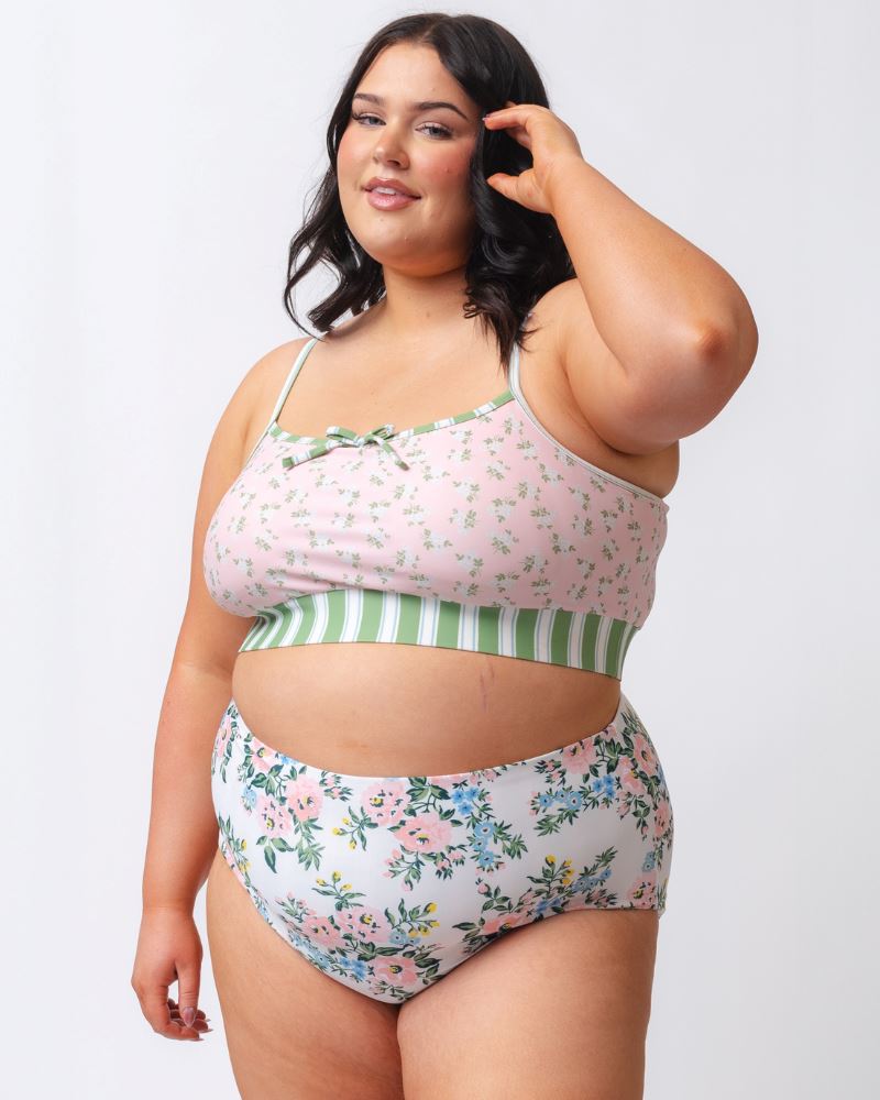 Photo of a woman wearing a pink and green floral swim bralette and a white and pink floral/ green striped reversible swim bottom- floral side