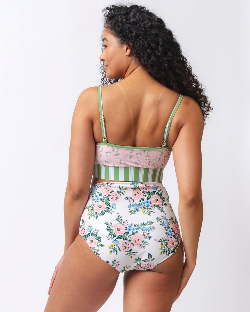 Photo of a woman with her back facing us wearing a pink floral cropped swim top with pink and white floral high waist swim bottoms