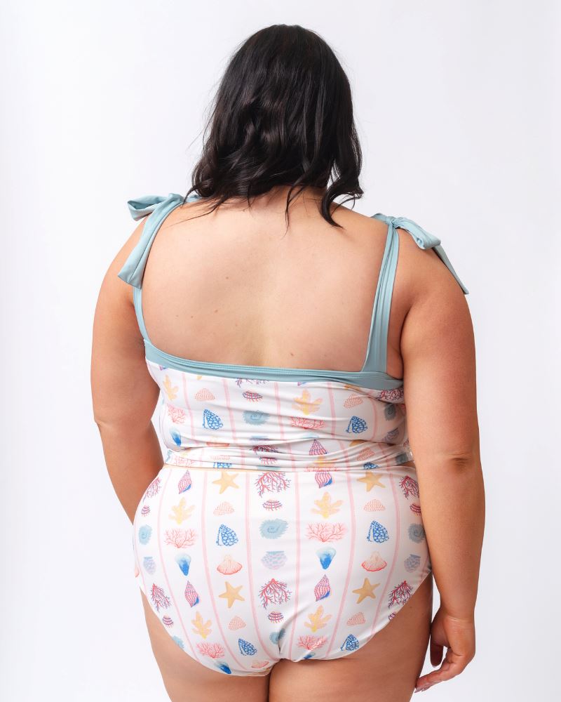 Photo of a woman wearing a seashell striped high waist swim bottom and a seashell striped shoulder-tie swim crop- back angle