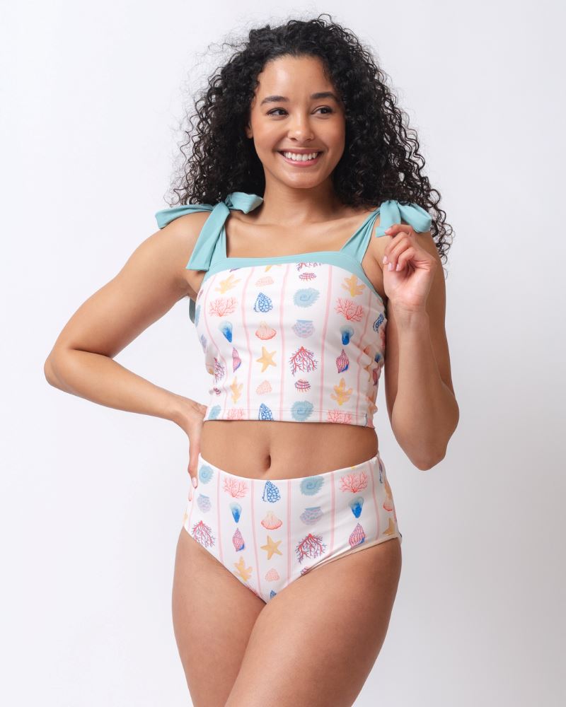 Photo of a woman wearing a seashell striped shoulder-tie swim crop top and a seashell striped high waist swim bottom