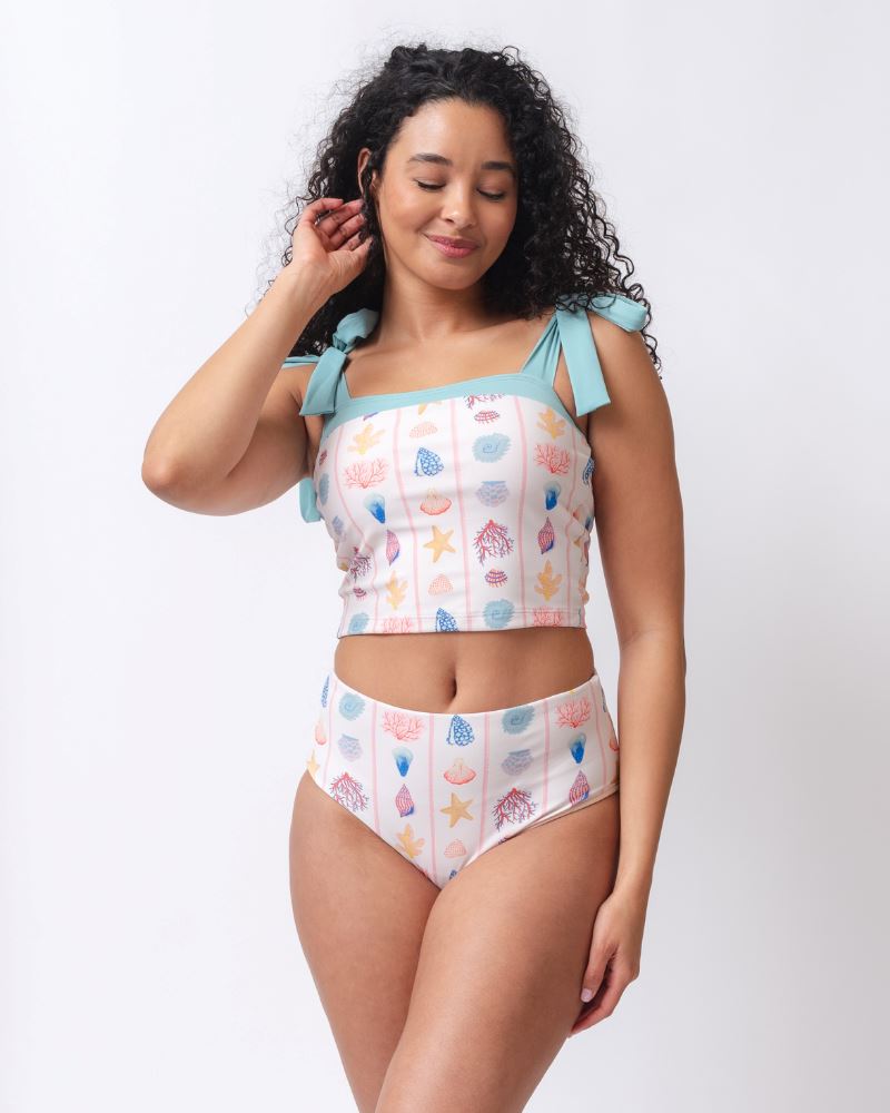 Photo of a woman wearing a seashell striped high waist swim bottom and a seashell striped shoulder-tie swim crop top