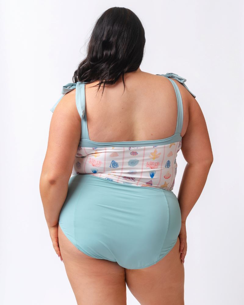 Photo of a woman wearing a seashell striped shoulder-tie swim crop top and a light blue high waist swim bottom- back angle