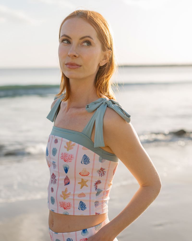 Close up photo of a woman posing on the beach wearing a seashell striped shoulder-tie swim crop top