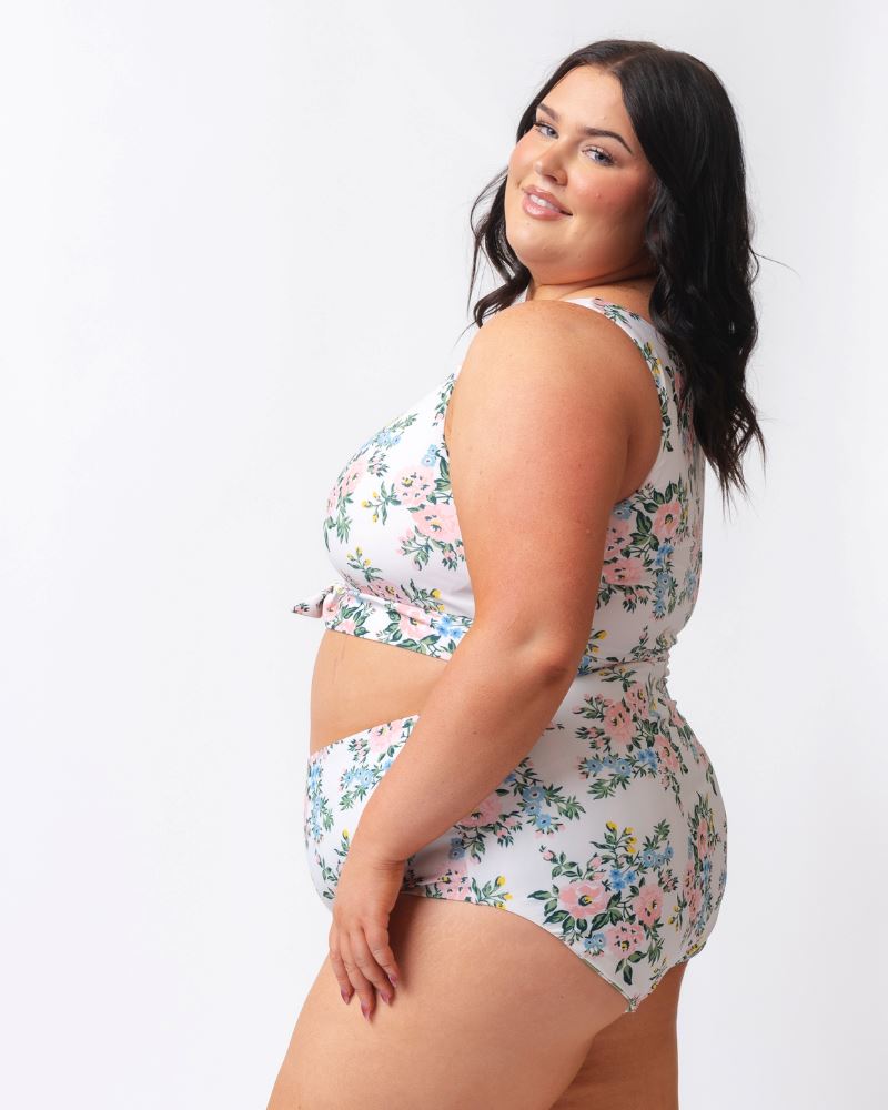 Photo of a woman from the side wearing a pink and white floral cropped swim top with pink and white floral high waist swim bottoms