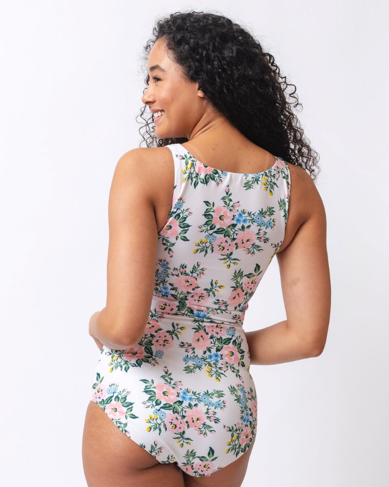 Photo of a woman with her back facing us wearing a pink and white floral cropped swim top with pink and white floral high waist swim bottoms