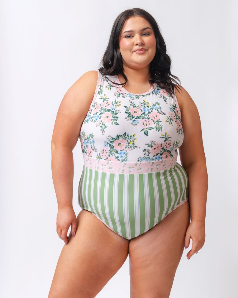 Photo of a woman wearing a pink and white floral with green and white stripes one piece swimsuit