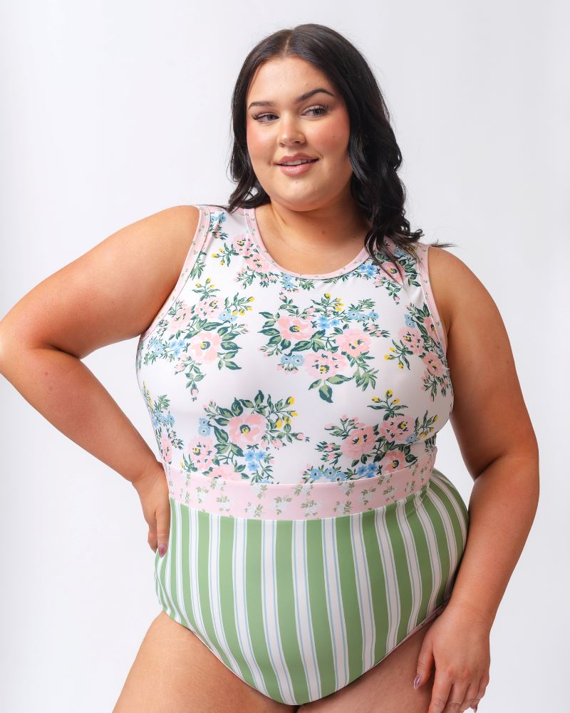 Photo of a woman wearing a pink and white floral with green and white stripes one piece swimsuit