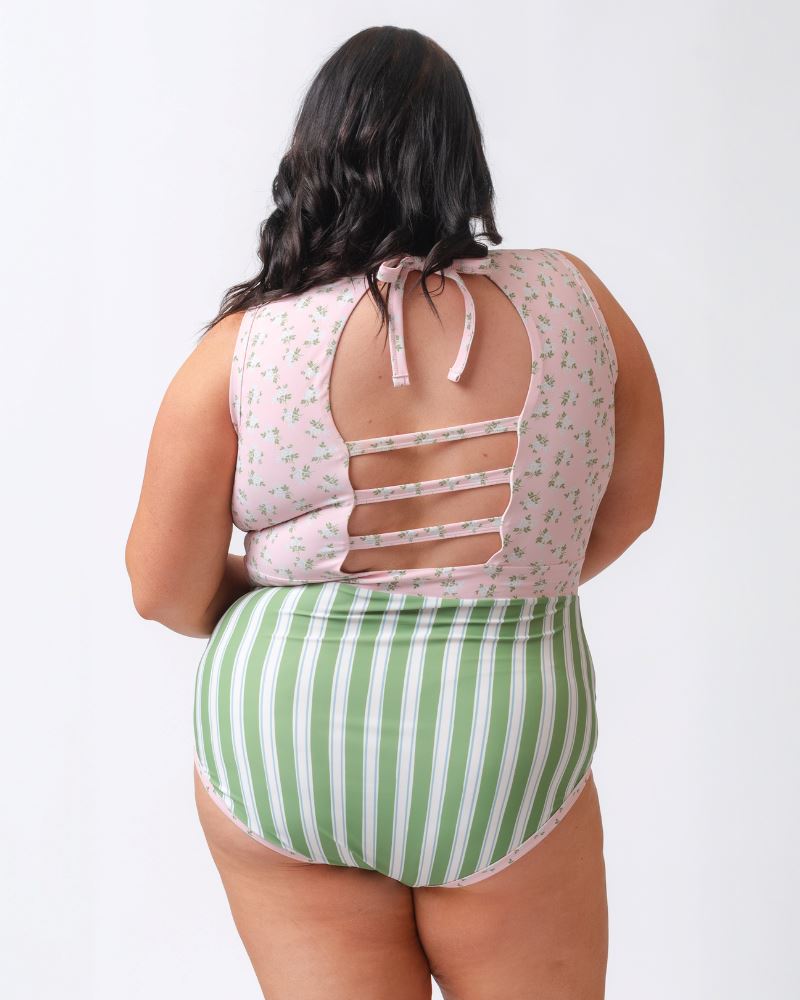 Photo of a woman with her back facing us wearing a pink and white floral with green and white stripes one piece swimsuit