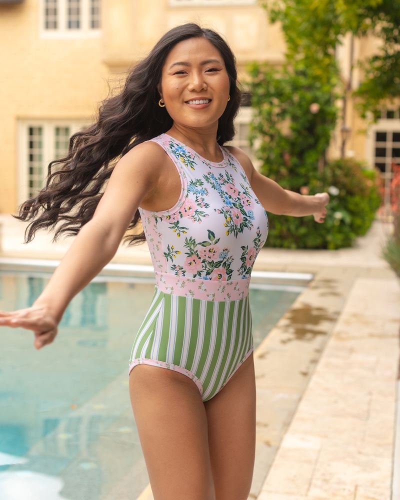 Photo of a woman wearing a pink and white floral with green and white stripes one piece swimsuit