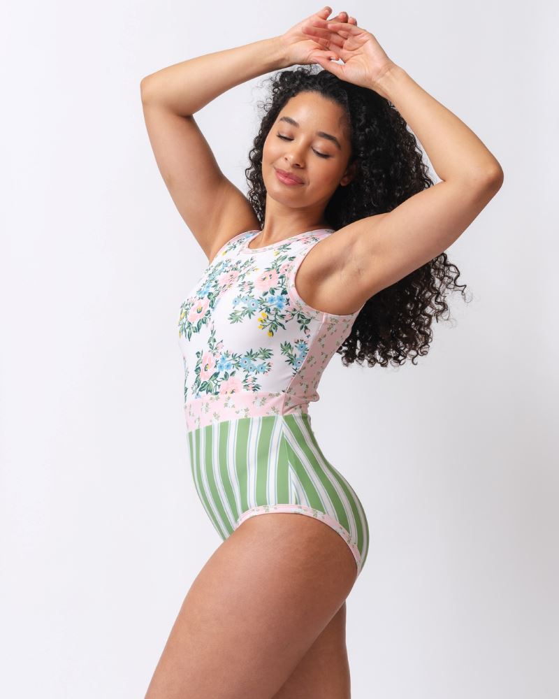 Photo of a woman from the side wearing a pink and white floral with green and white stripes one piece swimsuit