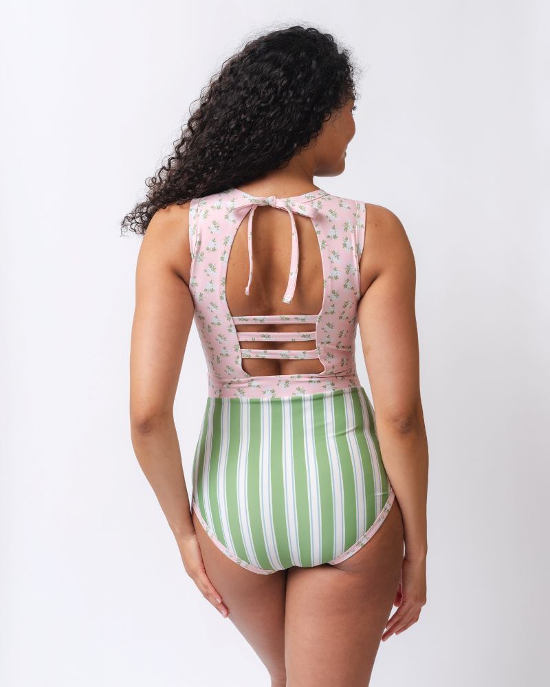 Photo of a woman with her back facing us wearing a pink and white floral with green and white stripes one piece swimsuit