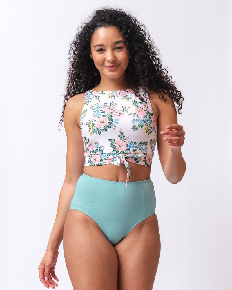 Photo of a woman wearing a light blue high waist swim bottom and a pink and white floral swim crop top