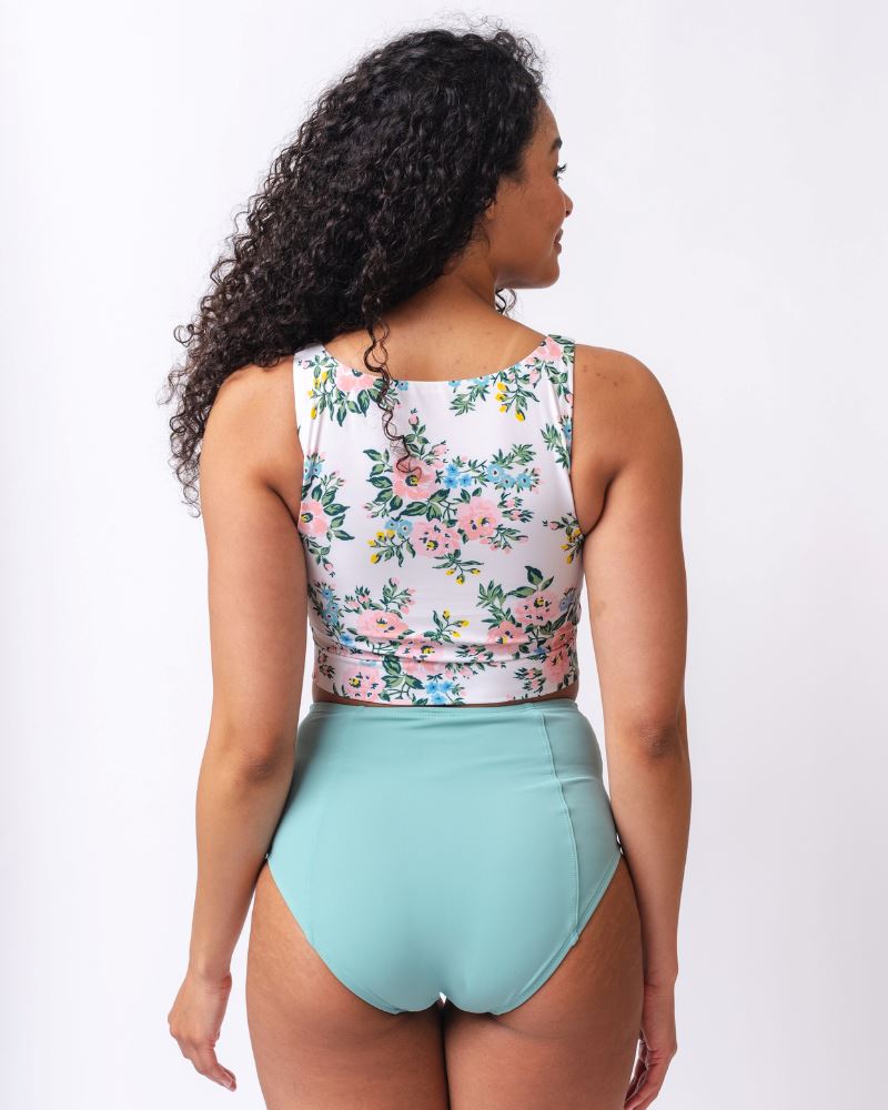 Photo of a woman wearing a light blue high waist swim bottom and a pink and white floral swim crop top- back angle