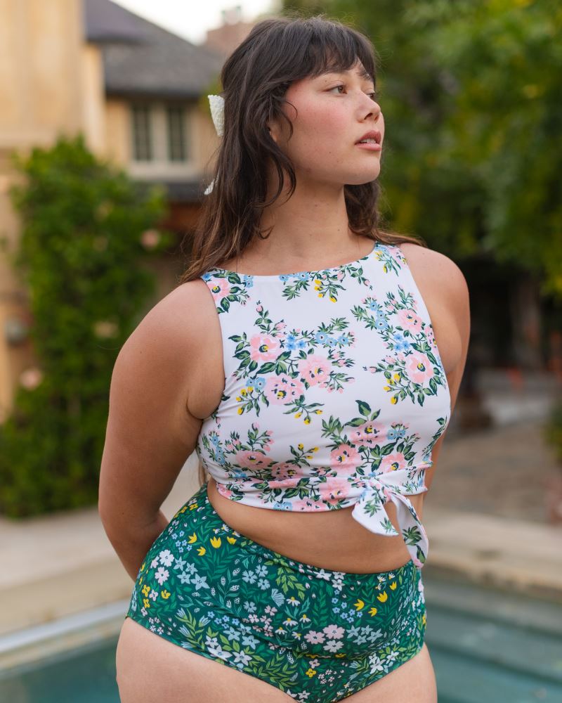 Photo of a woman wearing a pink and white floral cropped swim top with green floral high waist swim bottoms