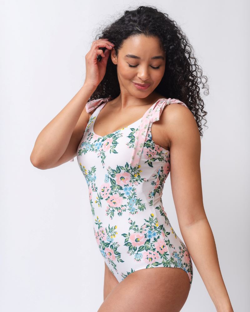Photo of a woman from the side wearing a pink and white floral one piece swimsuit