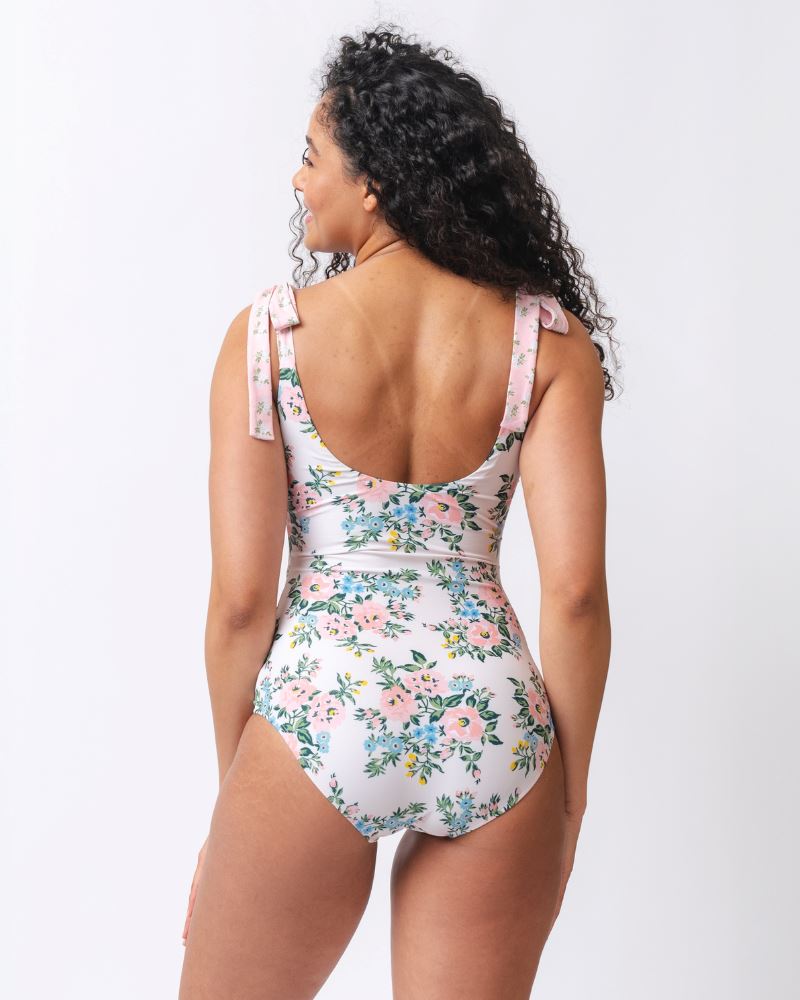 Photo of a woman with her back facing us wearing a pink and white floral one piece swimsuit