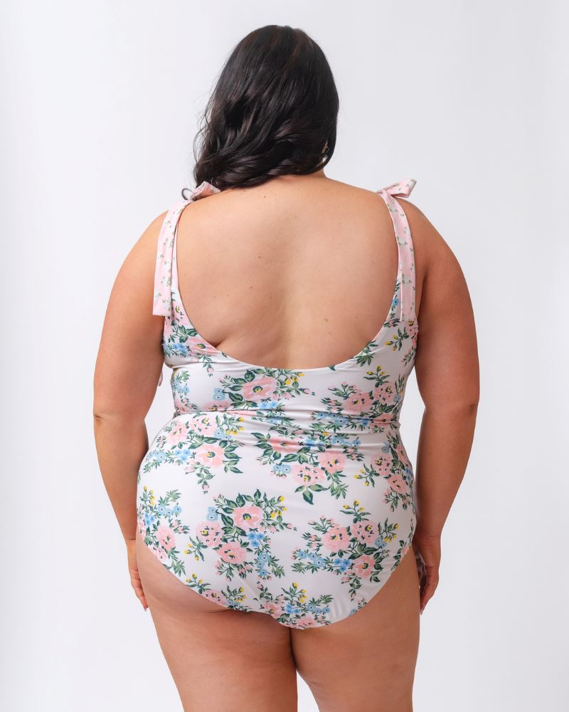 Photo of a woman with her back facing us wearing a pink and white floral one piece swimsuit