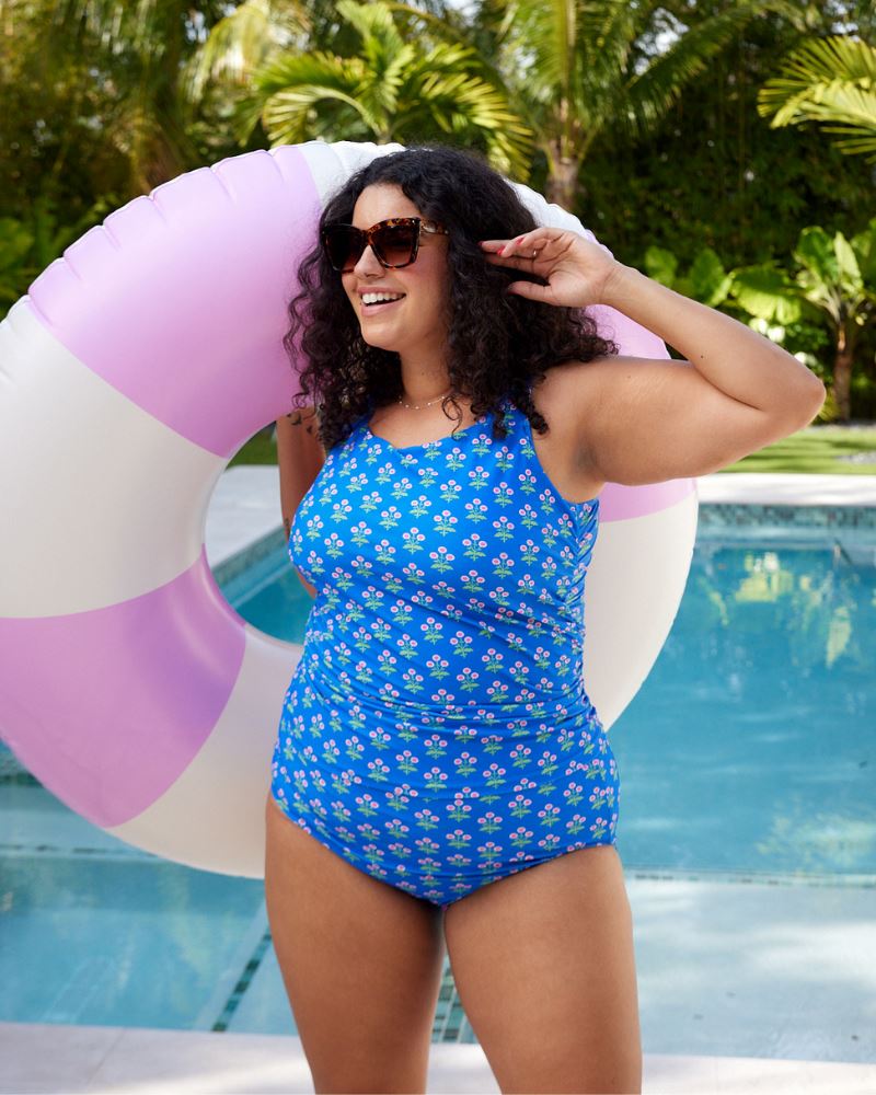 Photo of a woman holding a pool floatie by the pool wearing a blue floral print square neck swim tankini with a blue floral print high waist swim bottom