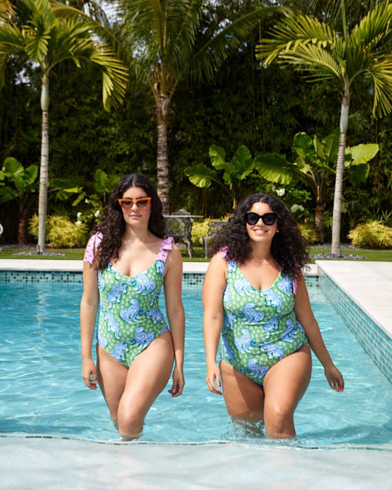 Photo of two women walking out of the pool wearing bold green and pink tiger print shoulder tie swim one pieces