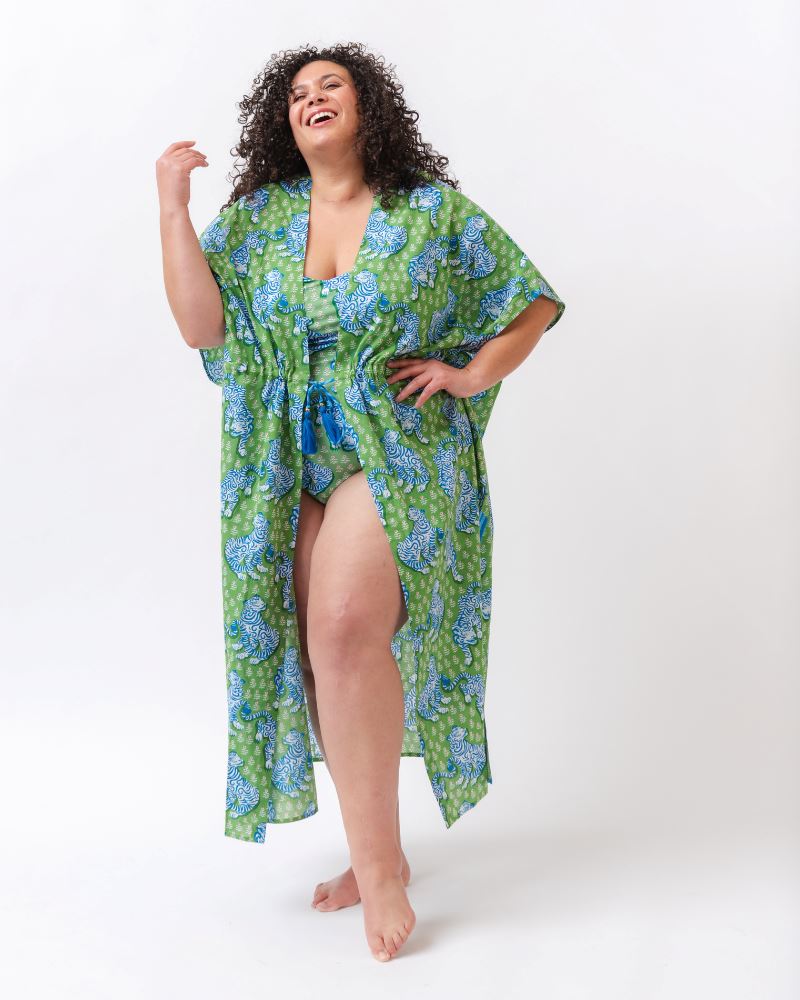 Photo of a woman wearing a bold green and pink tiger print shoulder tie swim one piece with a bold green tiger print long cover up