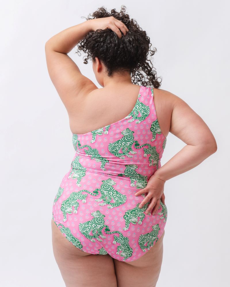 Photo of a woman with her back facing us wearing a bold pink and green tiger print one shoulder crop swim top with matching high waist swim bottoms