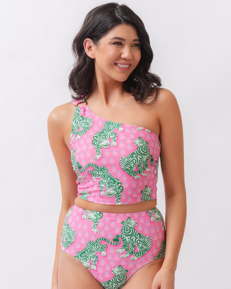 Photo of a woman wearing a bold pink and green tiger print one shoulder crop swim top with matching high waist swim bottoms