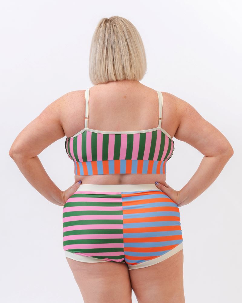 Photo of a woman wearing a multi-colored striped swim bralette and a multi-colored striped retro swim short bottom- back angle