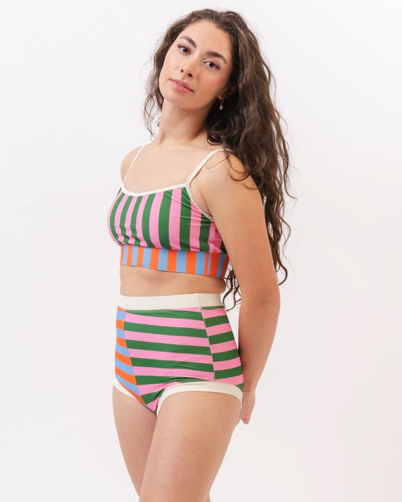 Photo of a woman wearing a multi-colored striped swim bralette and a multi-colored striped retro swim short bottom- side angle