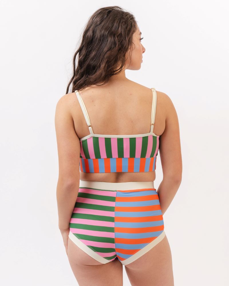 Photo of a woman wearing a multi-colored striped swim bralette and a multi-colored striped retro swim short bottom- back angle