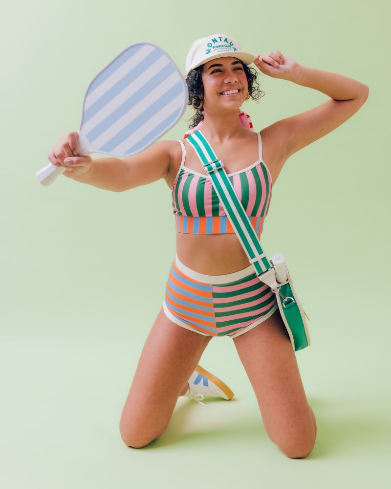 Photo of a woman posing with sports equipment wearing a multi-colored striped swim bralette and a multi-colored striped retro swim short bottom