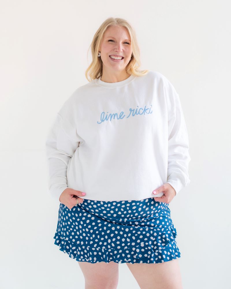 Photo of woman wearing a white Lime Ricki crew neck sweatshirt with a blue and white polka dot swim skirt