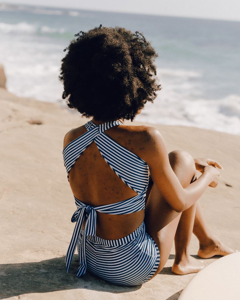 Photo of a woman wearing an Indigo stripe cross-back swim crop top and an Indigo stripe swim short bottom back angle