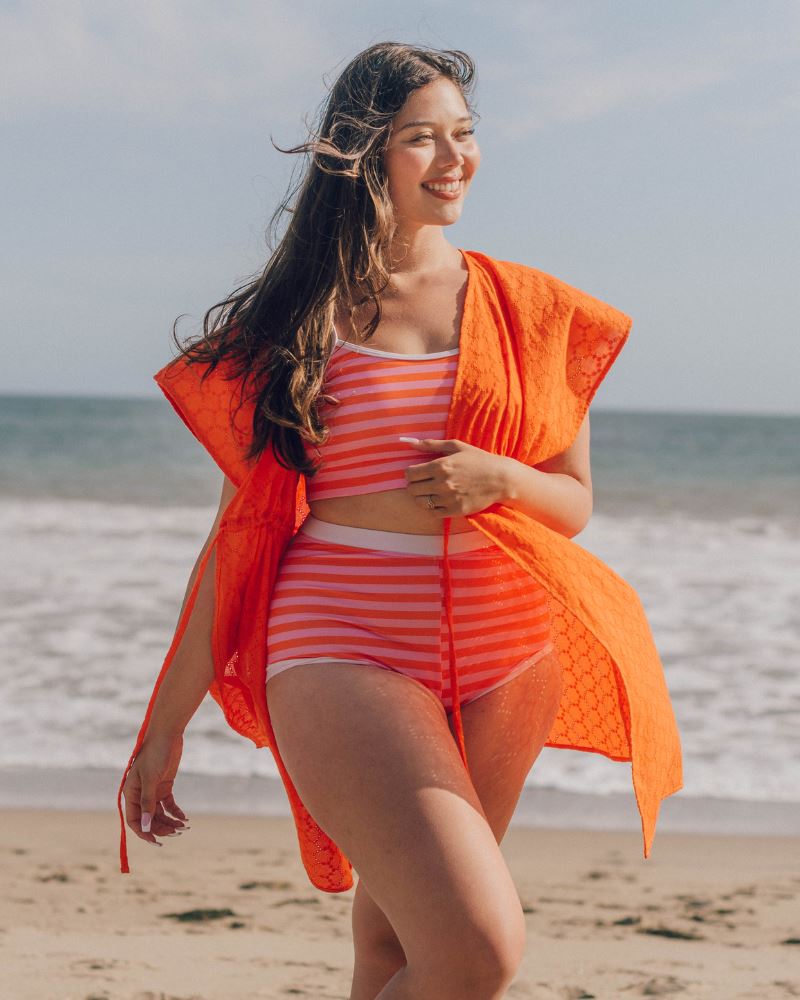 Photo of a woman wearing an orange Kaftan cover up and a pink and orange stripe swim bralette and a pink and orange stripe swim bottom