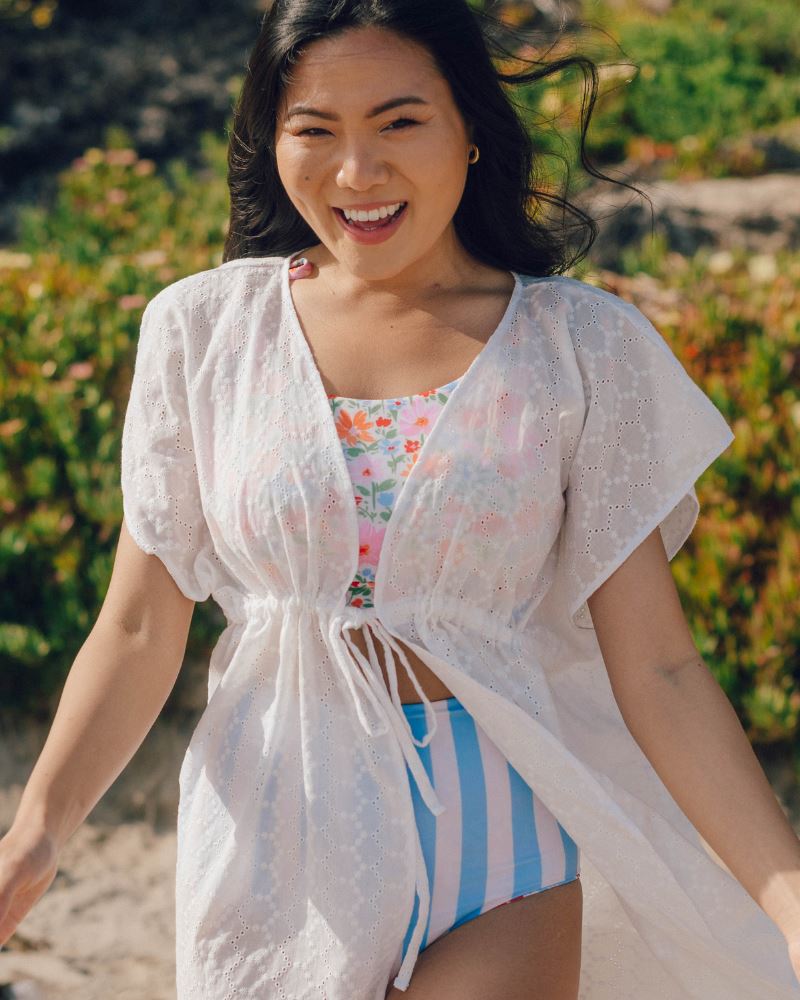 Photo of a woman wearing a white kaftan Cover-up and a floral swim crop top and a blue and white stripe swim bottom