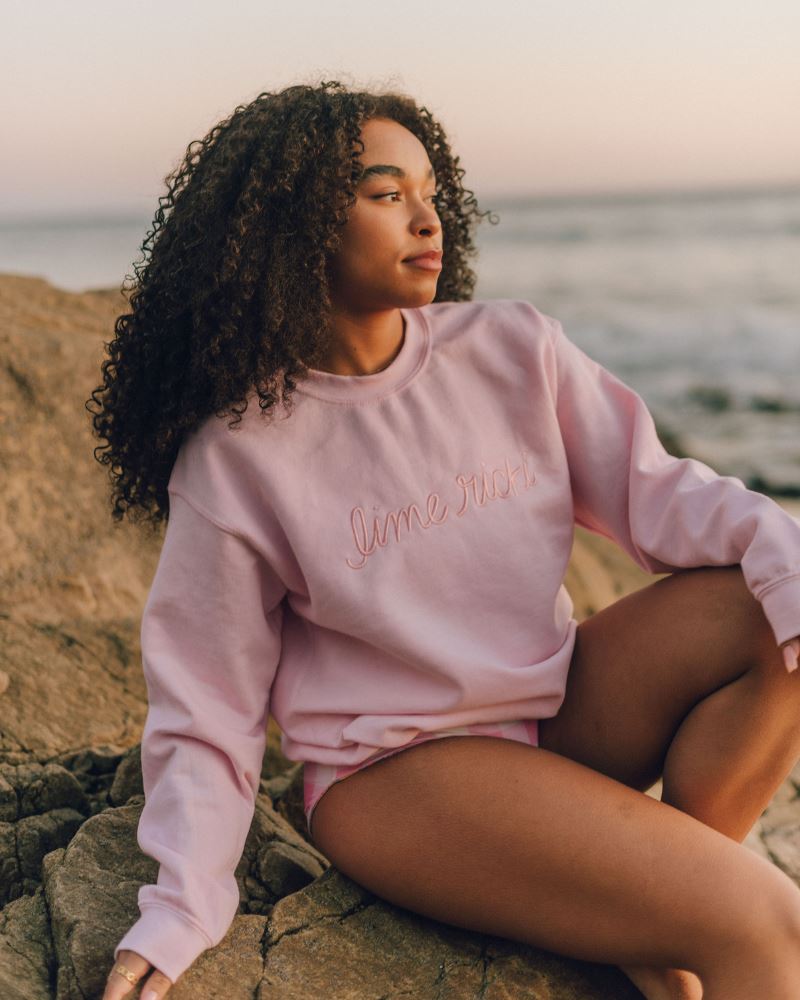 Photo of a woman wearing a pink crew neck sweatshirt and a pink checkered swim bottom