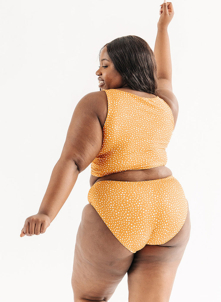 Photo of woman wearing orange and white dot cropped swim top with orange and white dot mid waist swim bottoms back angle