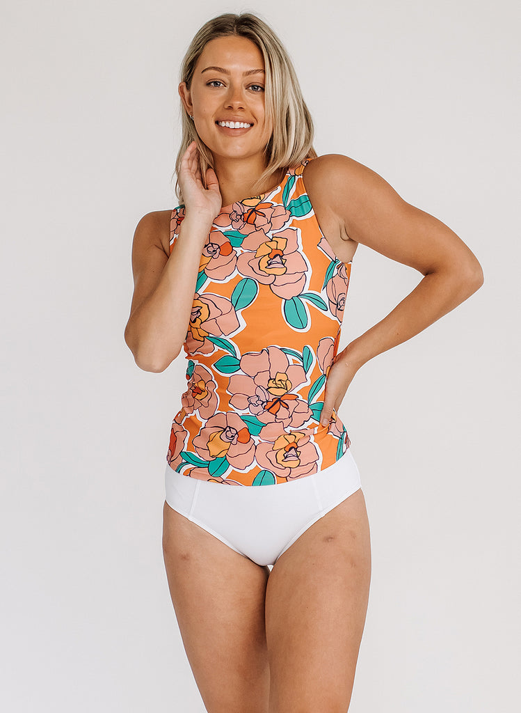 Photo of a woman wearing an orange floral swim top with white high waist swim bottoms