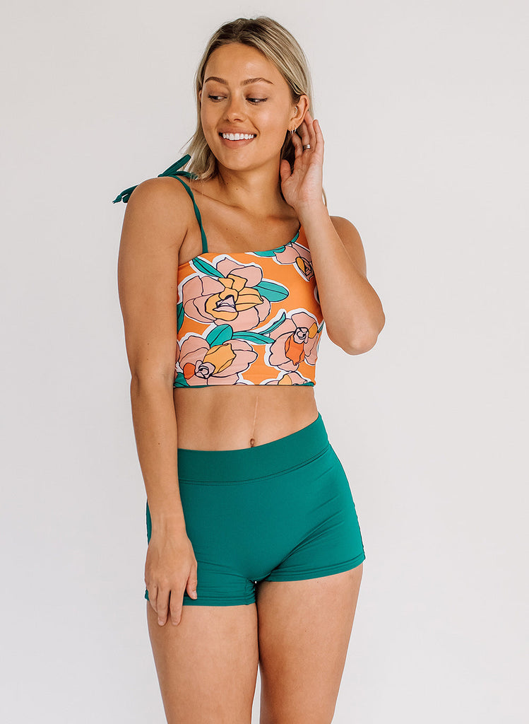 Photo of a woman wearing an orange floral cropped swim top with blue high waist swim shorts