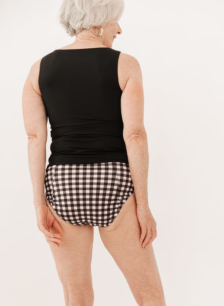 Photo of a woman wearing black gingham high-waist swim bottoms with a black boat neck swim top back angle