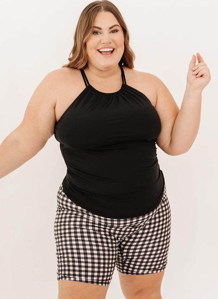 Photo of a woman wearing a black double cinch swim tankini top and black gingham swim shorts