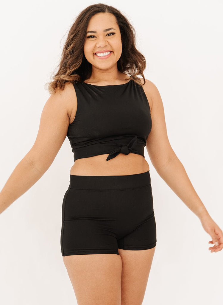 Photo of a woman wearing high-waist black swim shorts and a black knotted crop swim top