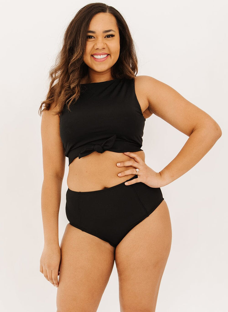 Photo of a woman wearing black high-waist swim bottoms with a black knotted crop swim top