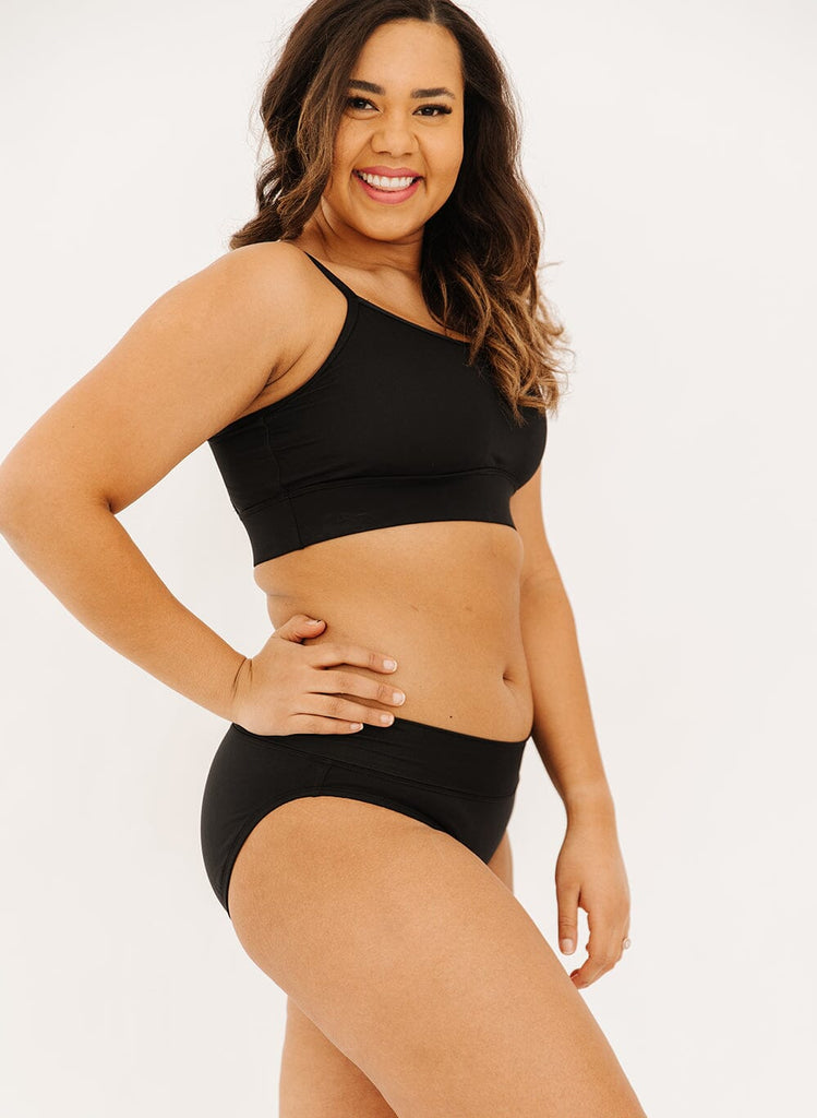 Photo of a woman in black classic swim bottoms and black swim bralette side angle