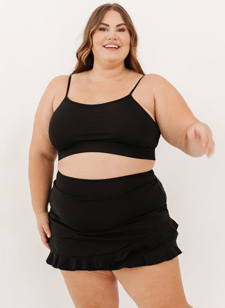 Photo of a woman wearing a black high-waist ruffle swim skirt with a black swim bralette