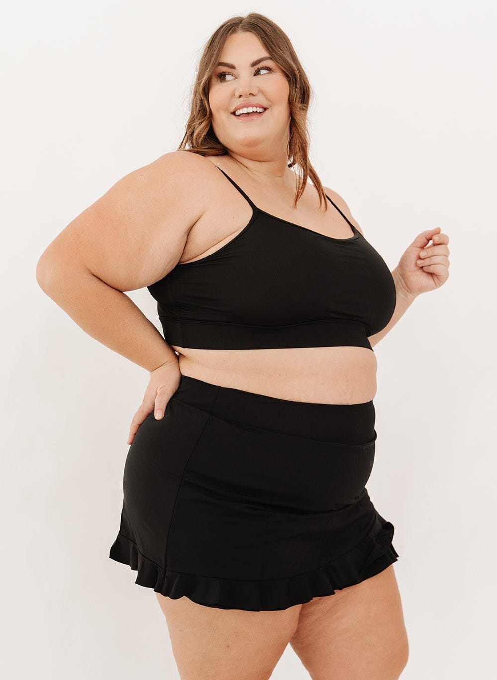 Woman wearing a black swim bralette and black swim skirt