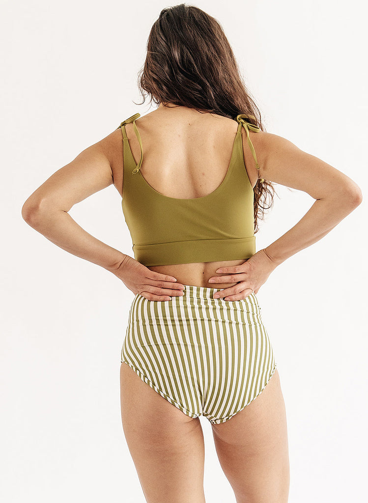 Photo of woman wearing green cropped swim top with green and white stripe swim bottoms back angle