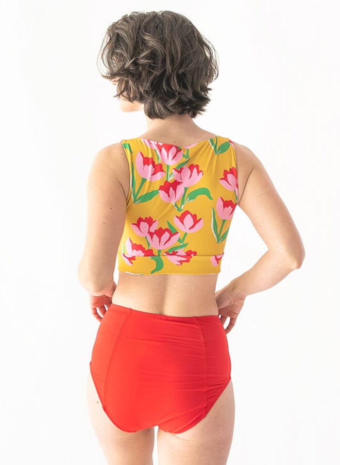 Photo of a woman wearing a red swim bottom and a yellow floral swim crop top back angle