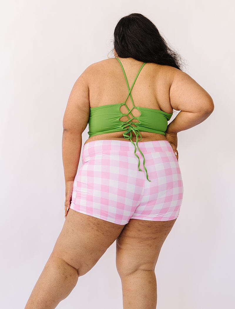Photo of woman wearing green lace back swim top with pink gingham swim shorts back angle