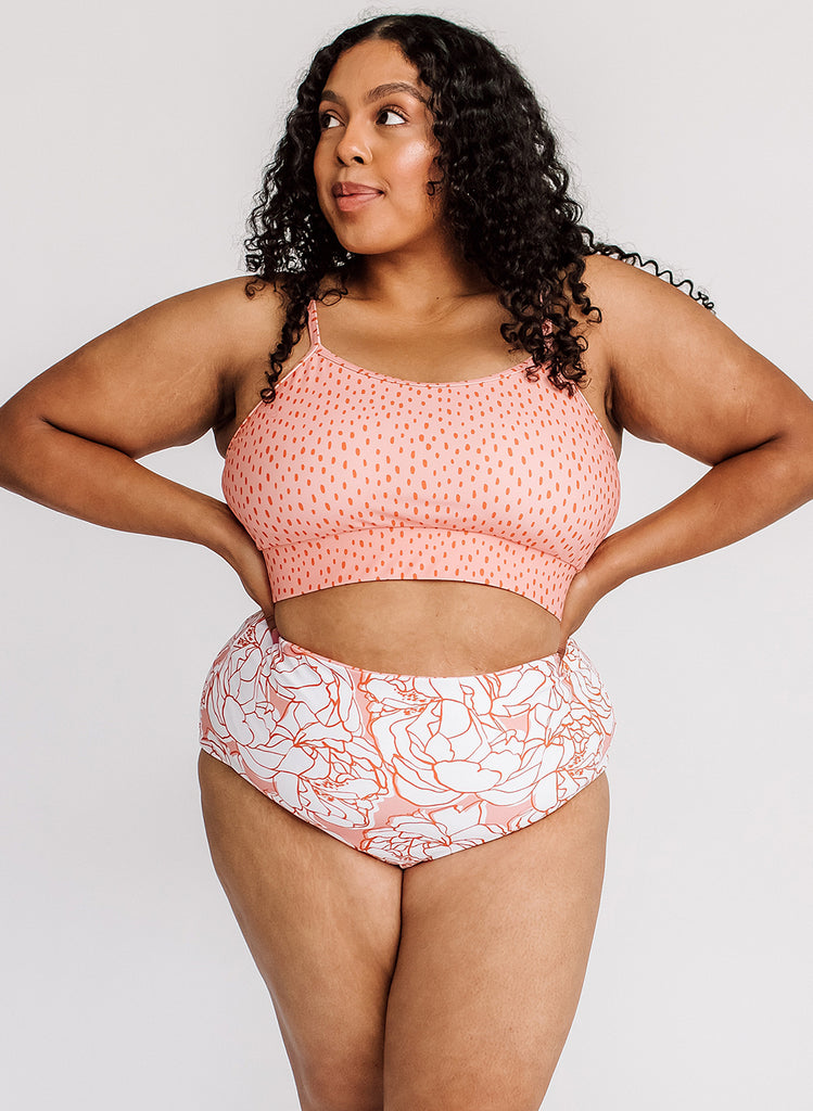 Photo of woman with her hands on her hips wearing a pink polka dot cropped swim top with pink and white floral high waist swim bottoms