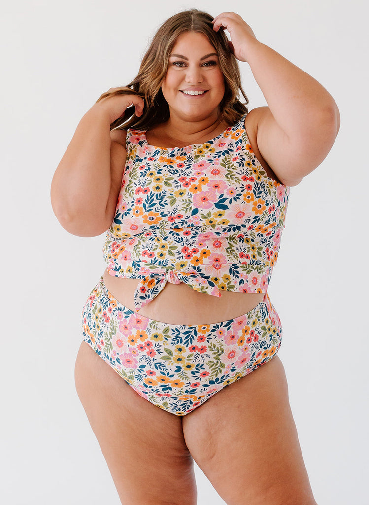 Photo of a woman with her hands in her hair wearing a multi colored floral cropped swim top with multi colored floral high waist swim bottoms